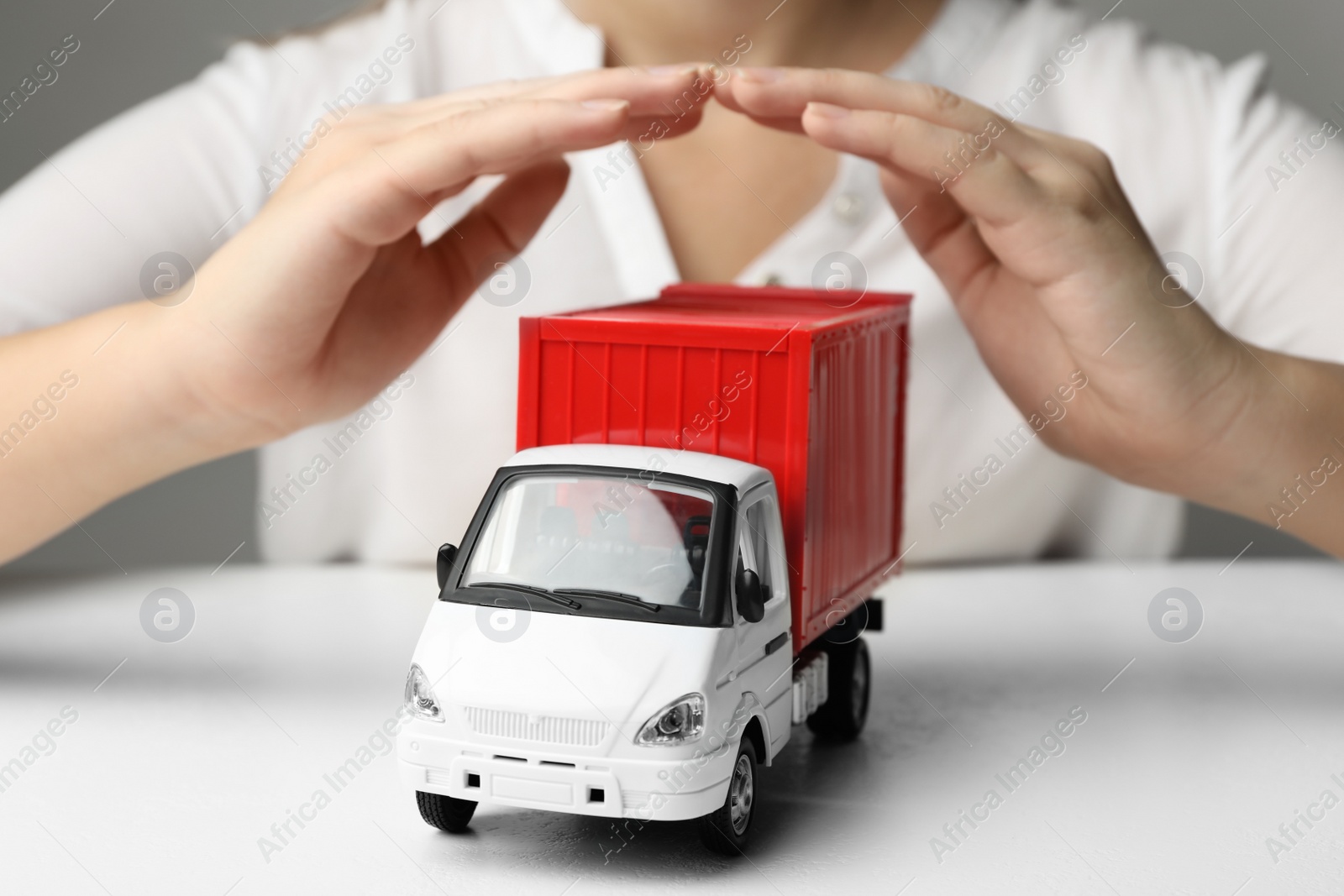 Photo of Woman covering toy truck at white table, closeup. Logistics and wholesale concept