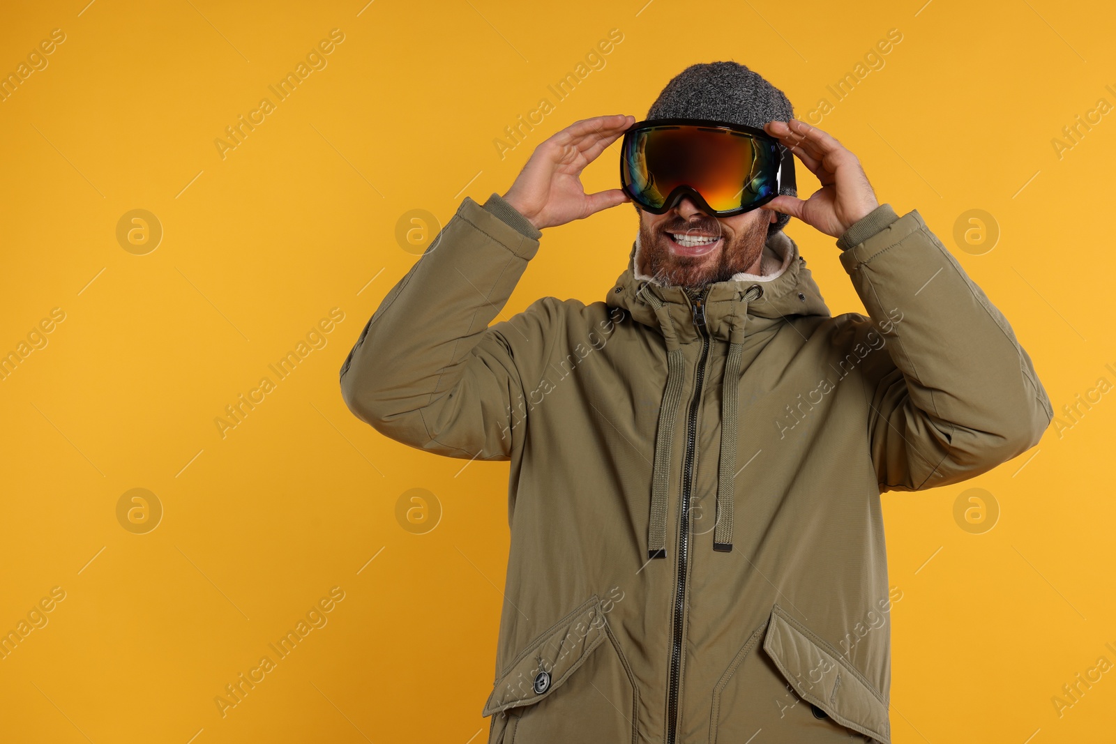 Photo of Winter sports. Happy man in ski suit and goggles on orange background, space for text
