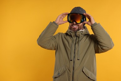 Photo of Winter sports. Happy man in ski suit and goggles on orange background, space for text