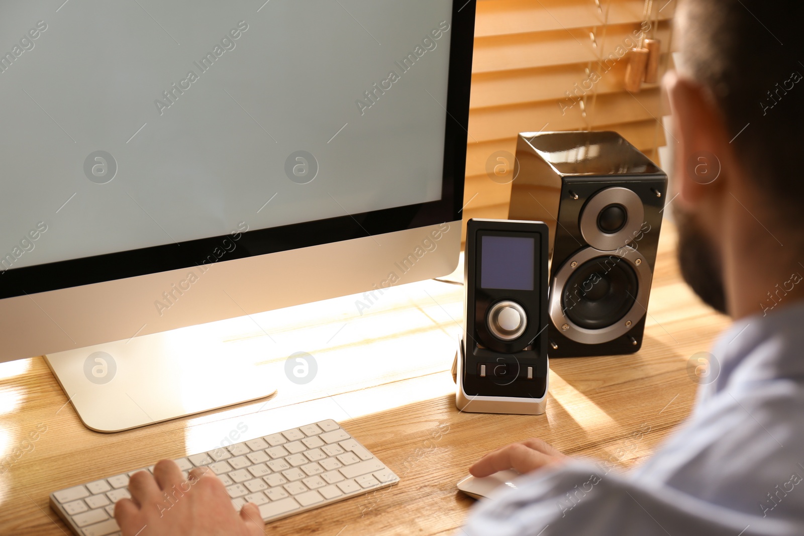 Photo of Man working on computer at wooden table indoors, closeup. Audio speaker system