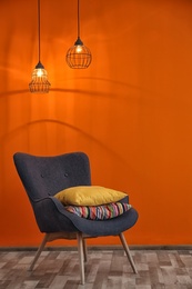 Photo of Armchair with different pillows near color wall in room