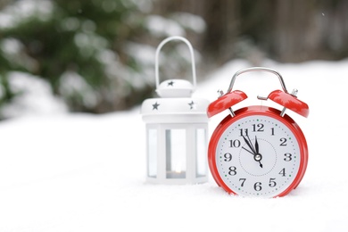 Photo of Lantern and red alarm clock on white snow outdoors. Space for text