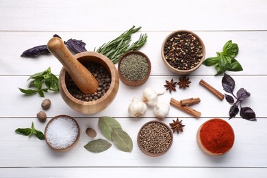 Mortar with pestle and different spices on white wooden table, flat lay