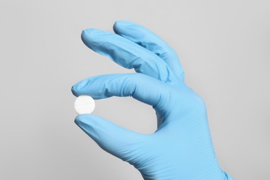 Doctor holding pill on grey background, closeup