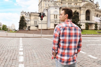 Photo of Young man waiting to cross street, back view. Traffic rules and regulations