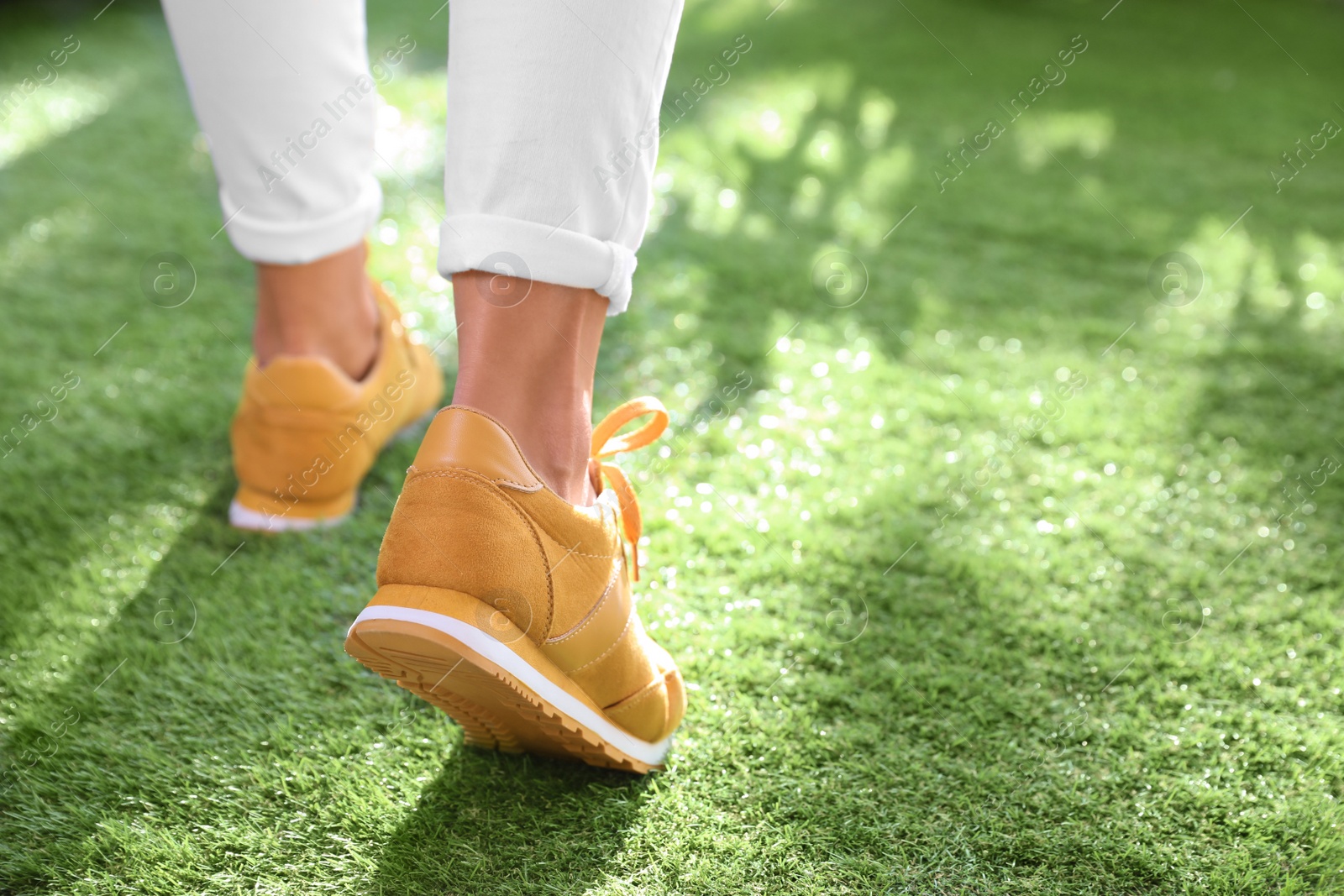 Photo of Young woman wearing stylish sneakers on green grass, closeup