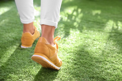 Photo of Young woman wearing stylish sneakers on green grass, closeup