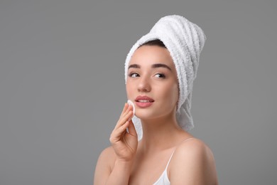 Photo of Beautiful woman in terry towel removing makeup with cotton pad on gray background, space for text