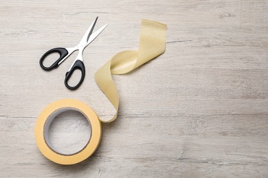 Photo of Roll of adhesive tape and scissors on wooden background, flat lay. Space for text