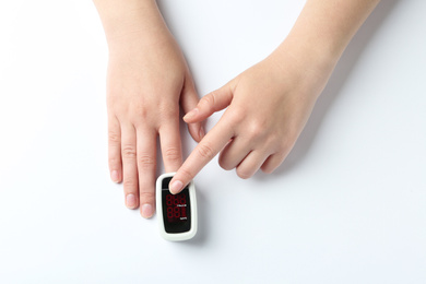 Woman using fingertip pulse oximeter on white background, top view