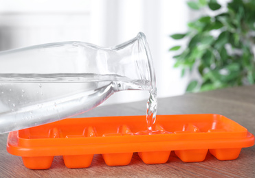 Photo of Woman pouring water into ice cube tray at wooden table, closeup