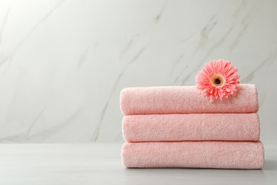 Stack of fresh towels with flower on grey table against light background. Space for text