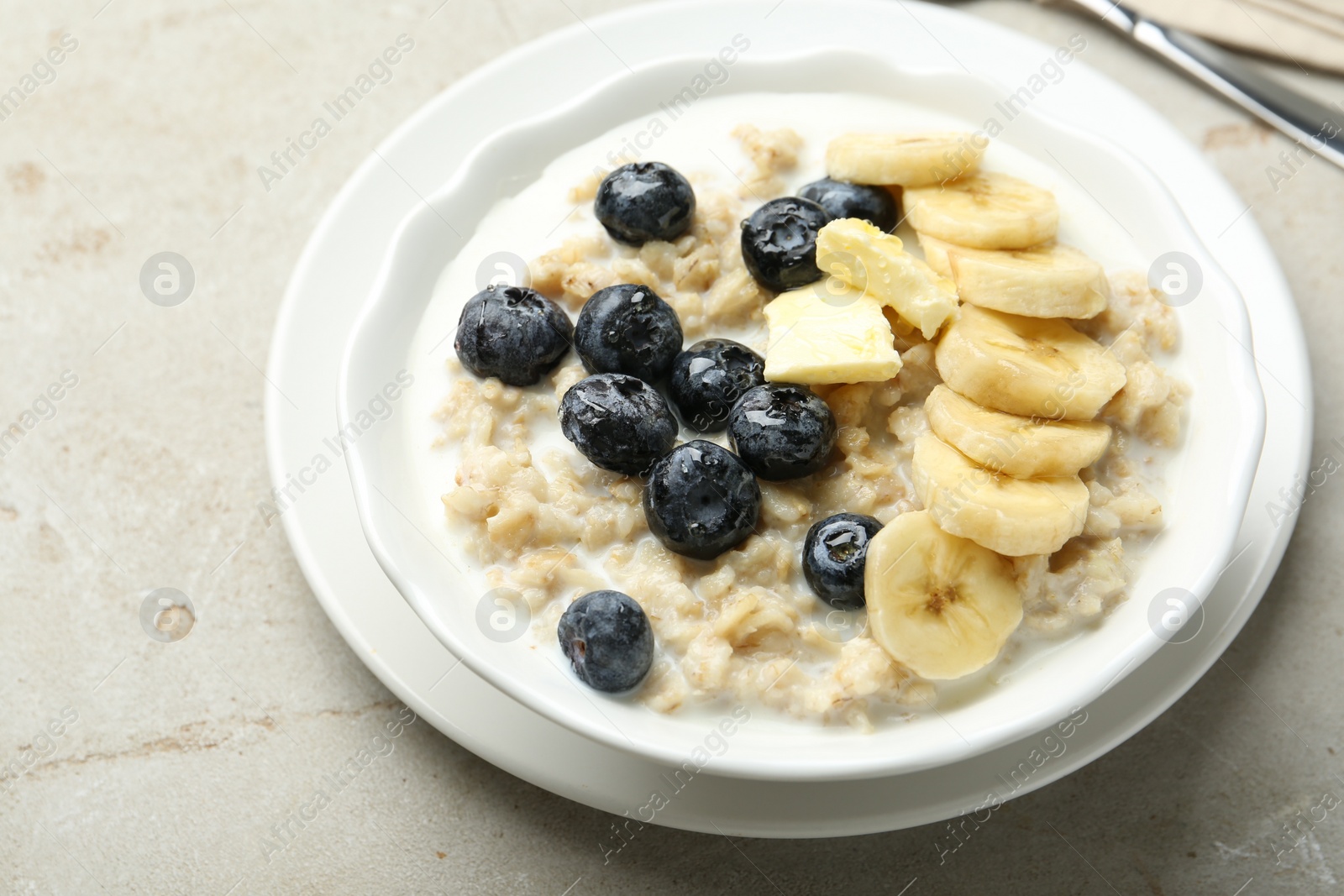 Photo of Tasty oatmeal with banana, blueberries, butter and milk served in bowl on light grey table