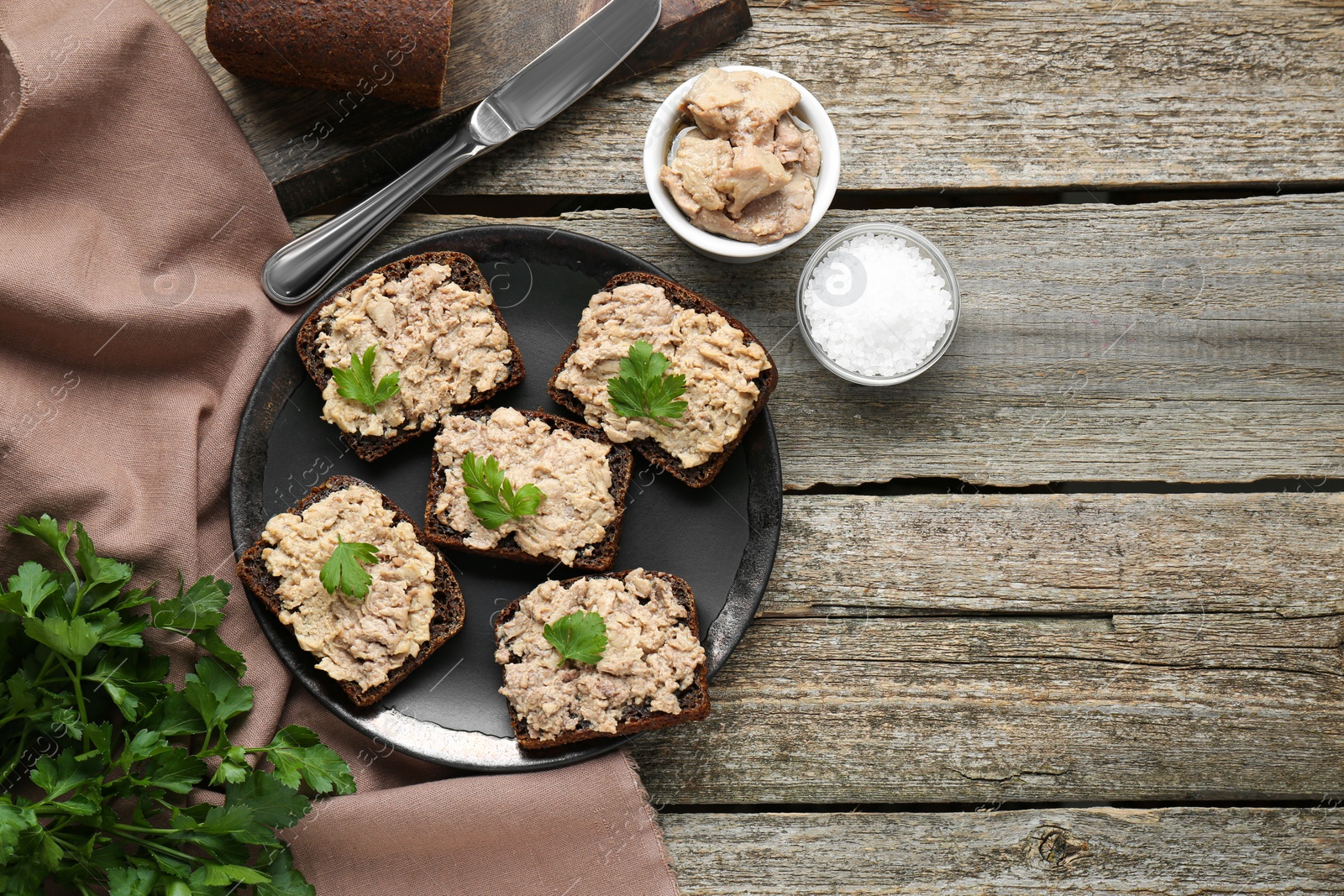 Photo of Tasty sandwiches with cod liver, salt and parsley on wooden table, flat lay. Space for text