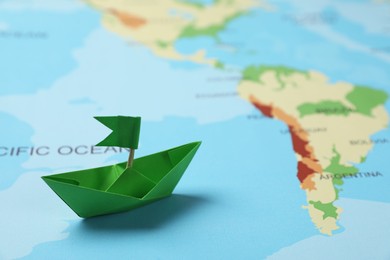 Photo of Green paper boat with flag on world map. Space for text