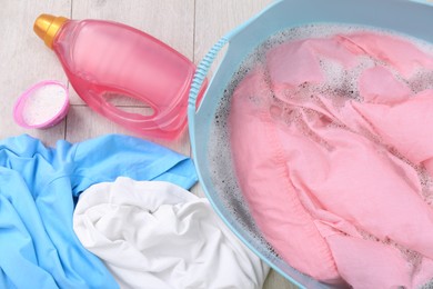 Photo of Basin with pink shirt near bottle of detergent and powder on floor, flat lay. Hand washing laundry