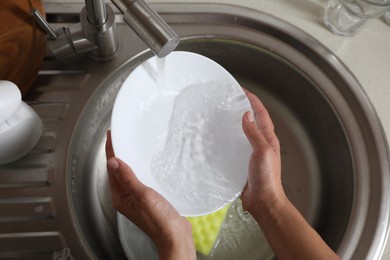 Photo of Woman washing plate in kitchen sink, above view