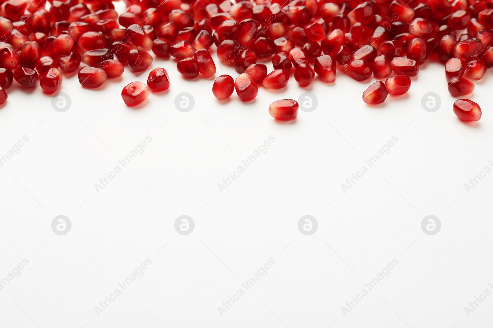 Photo of Many ripe juicy pomegranate grains on white background. Space for text