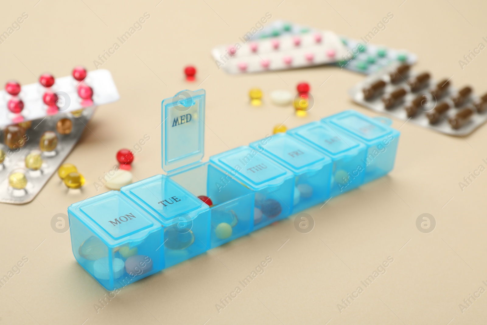 Photo of Plastic box with different pills on beige background