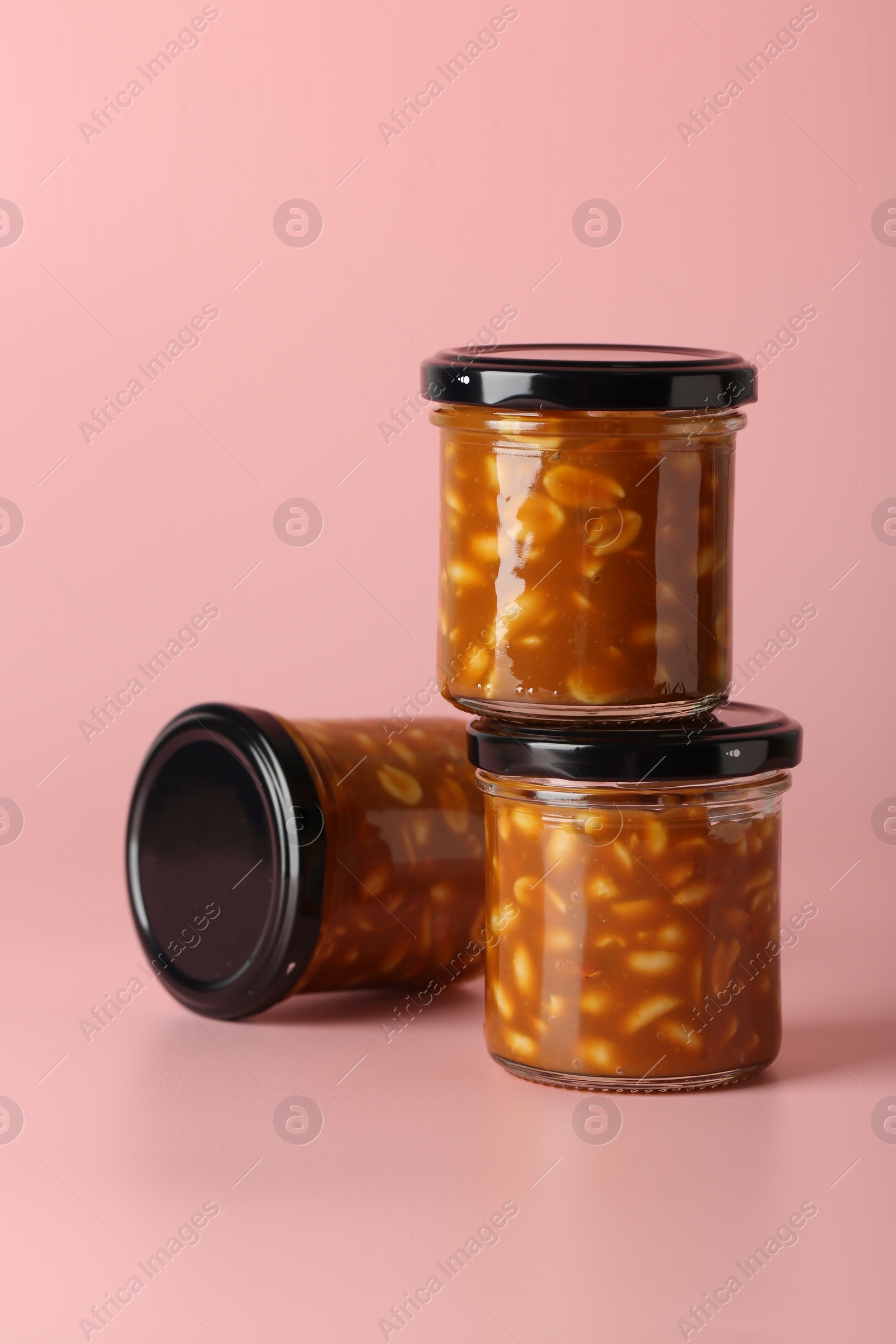 Photo of Tasty salted caramel with peanuts in jars on pink background