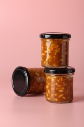 Photo of Tasty salted caramel with peanuts in jars on pink background