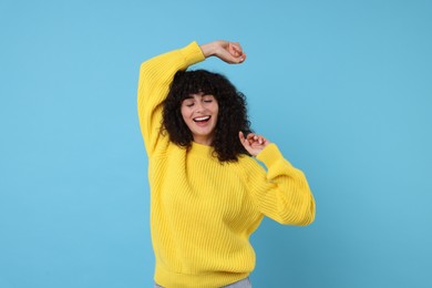 Happy young woman in stylish yellow sweater on light blue background