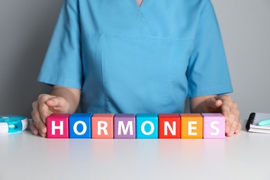 Doctor near word HORMONES made with colorful cubes at white table, closeup