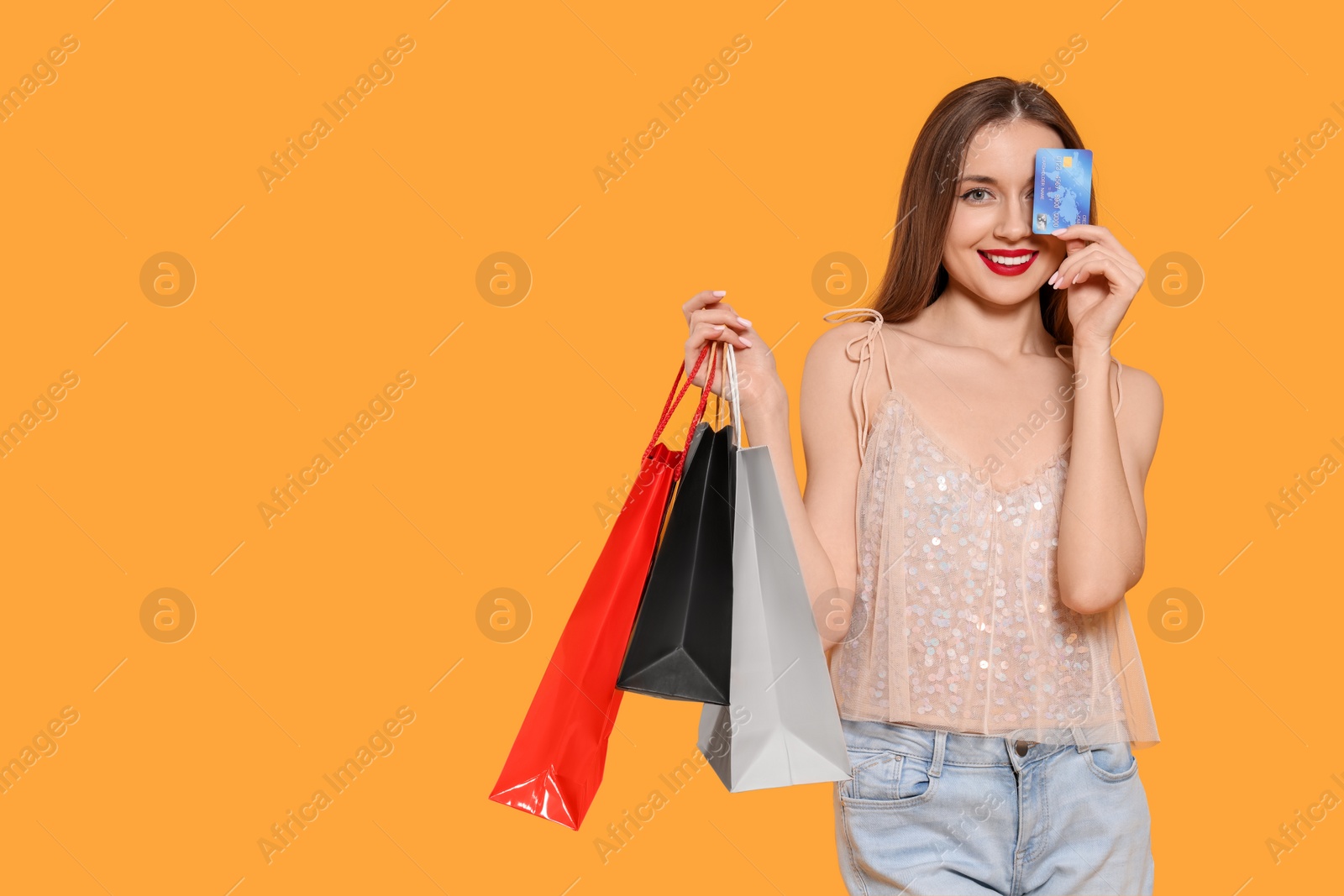 Photo of Stylish young woman with shopping bags and credit card on orange background, space for text