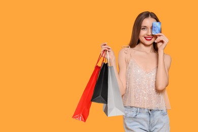 Stylish young woman with shopping bags and credit card on orange background, space for text