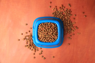 Dry pet food in feeding bowl on orange background, flat lay