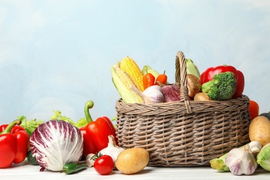 Photo of Fresh vegetables and wicker basket on white wooden table