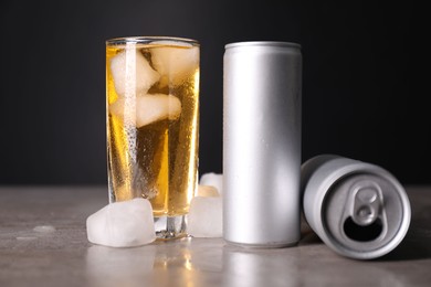 Tasty energy drink with ice cubes in glass and aluminium cans on grey table