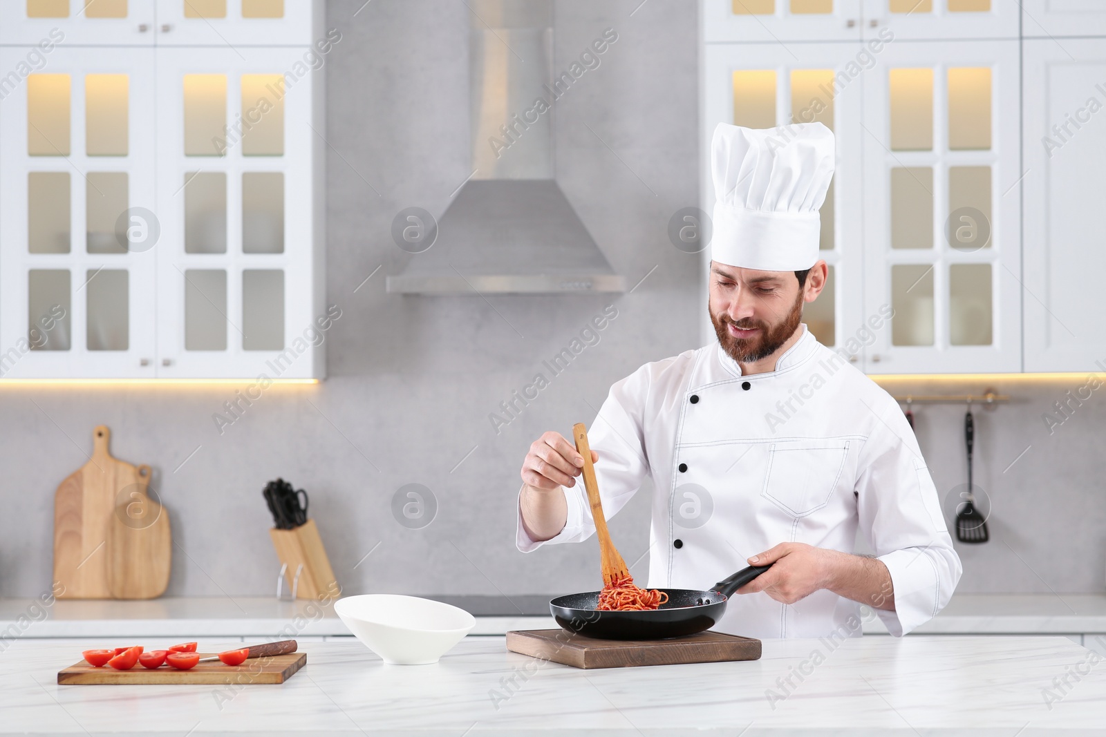 Photo of Professional chef with delicious spaghetti at marble table in kitchen