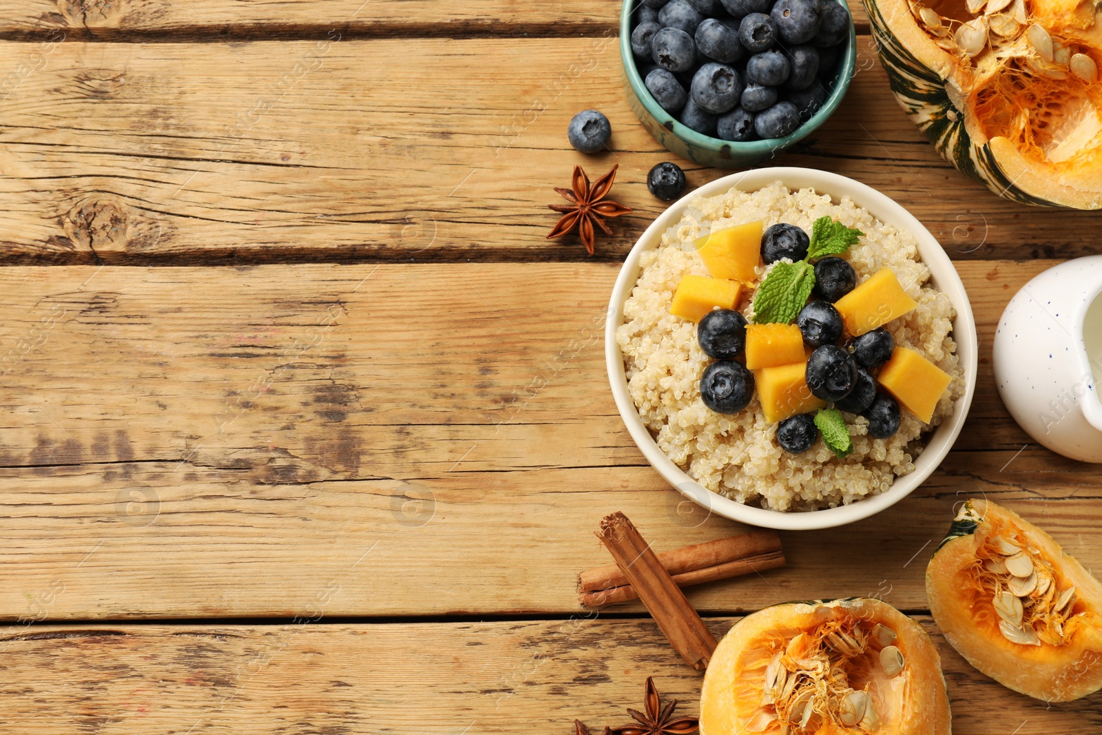 Photo of Flat lay composition with bowl of tasty quinoa porridge, blueberries and pumpkin on wooden table. Space for text