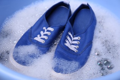 Photo of Washing pair of sport shoes in plastic basin, closeup