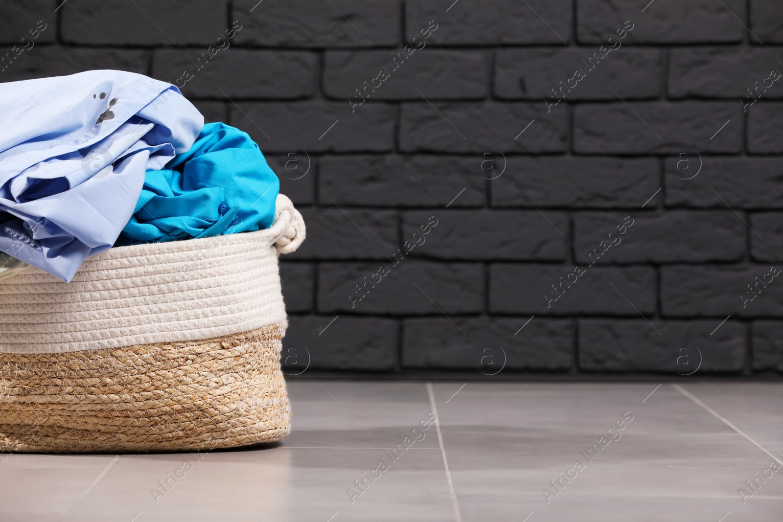 Photo of Laundry basket with clothes near black brick wall. Space for text