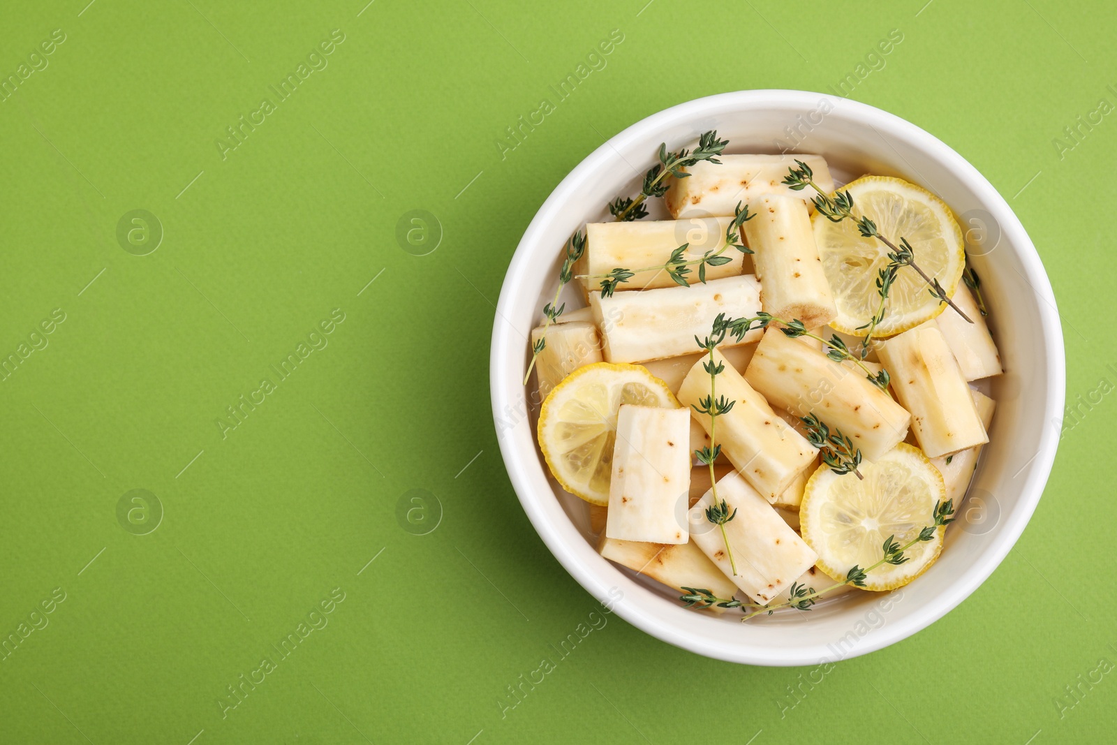 Photo of Dish with raw salsify roots, lemon and thyme on green table, top view. Space for text