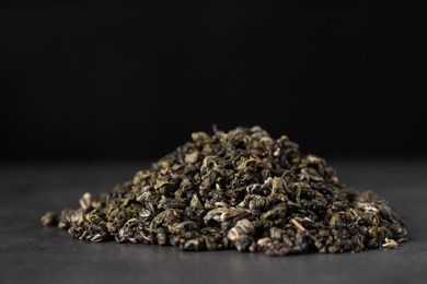 Photo of Heap of dried green tea leaves on grey table, closeup