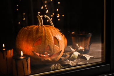 Photo of Composition with pumpkin head on windowsill, view through glass. Jack lantern - traditional Halloween decor