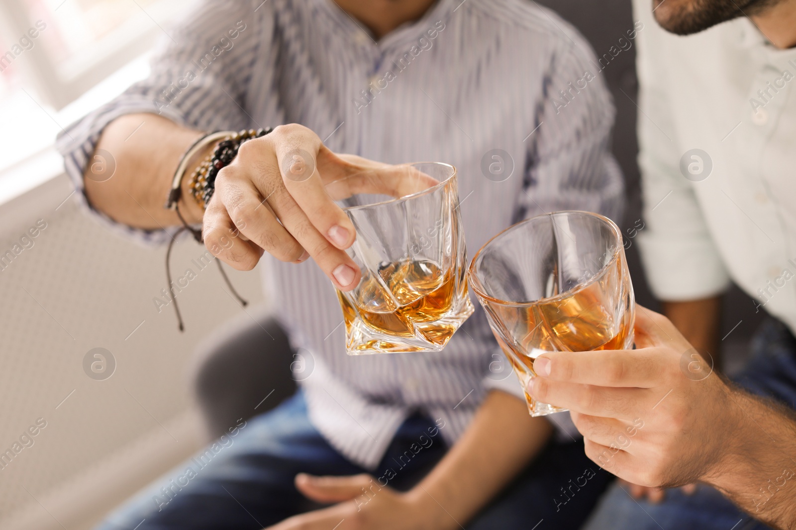 Photo of Friends toasting with glasses of whiskey indoors, closeup