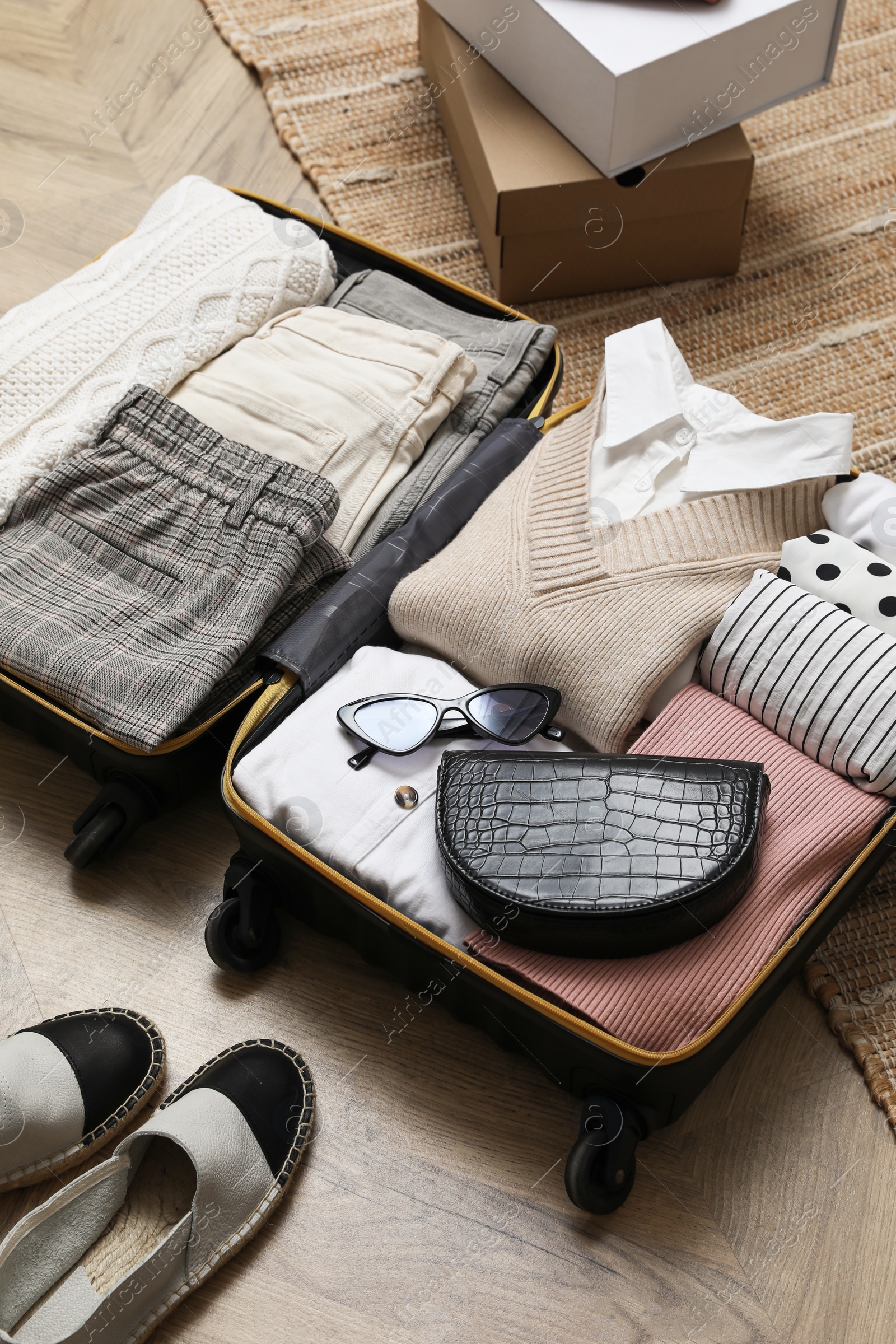 Photo of Open suitcase with folded clothes, accessories and shoes on floor