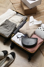 Open suitcase with folded clothes, accessories and shoes on floor