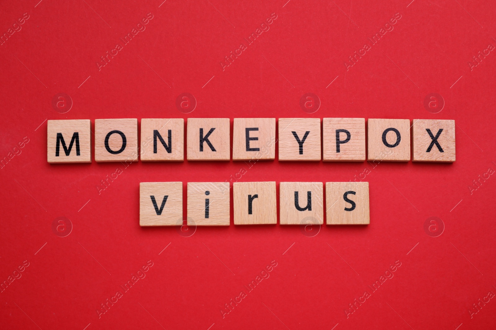 Photo of Words Monkeypox Virus made of wooden cubes on red background, top view