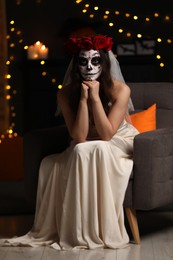 Young woman in scary bride costume with sugar skull makeup against blurred lights indoors. Halloween celebration