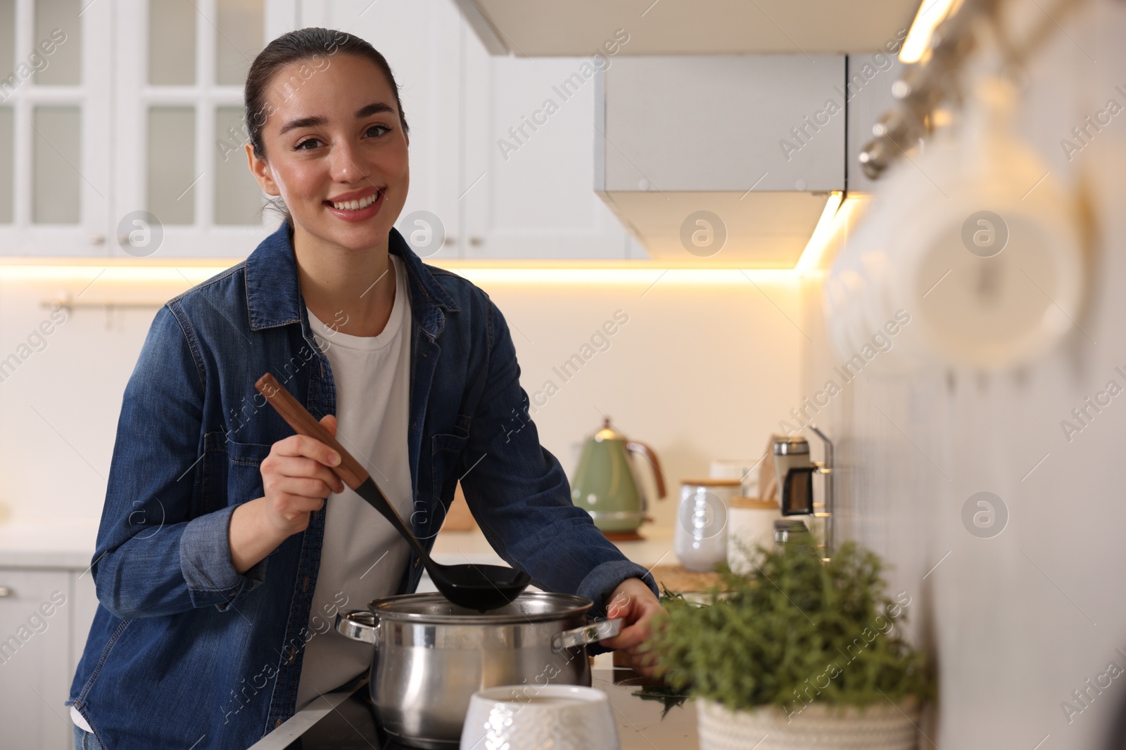 Photo of Smiling woman with ladle cooking soup in kitchen