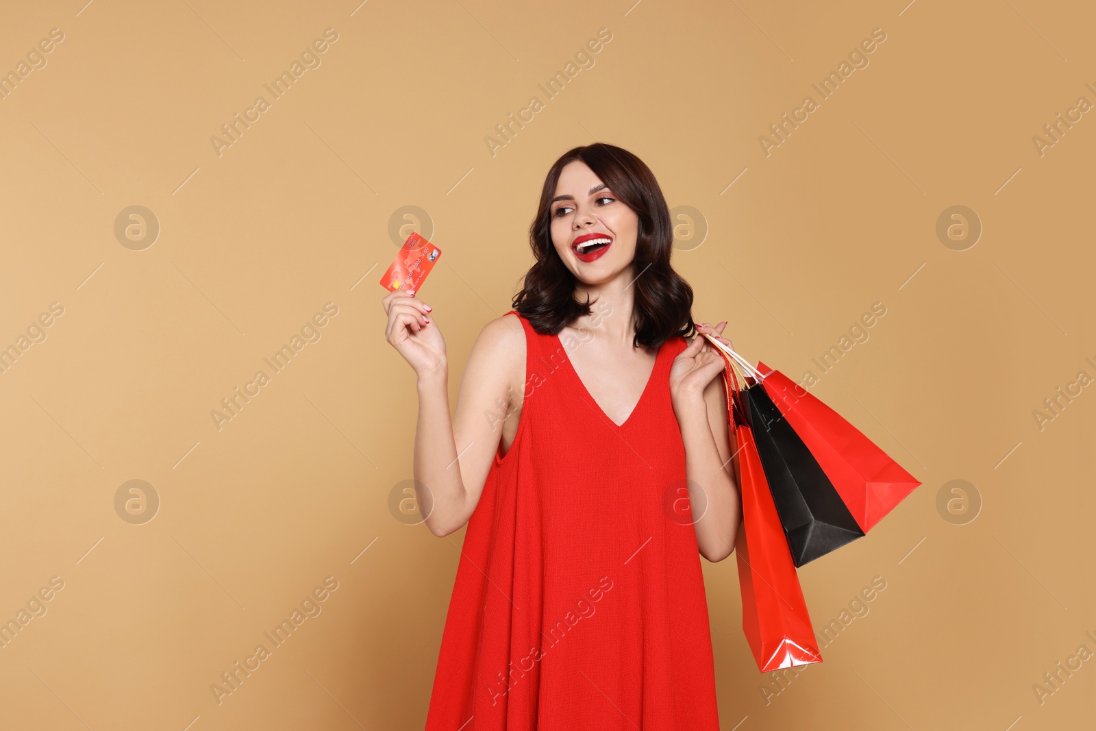 Photo of Beautiful young woman with paper shopping bags and credit card on beige background