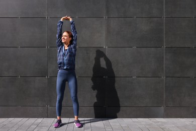 Beautiful woman in gym clothes doing exercises on street, space for text