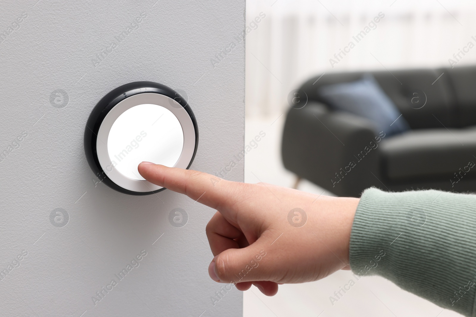 Photo of Man adjusting thermostat on white wall indoors, closeup. Smart home system