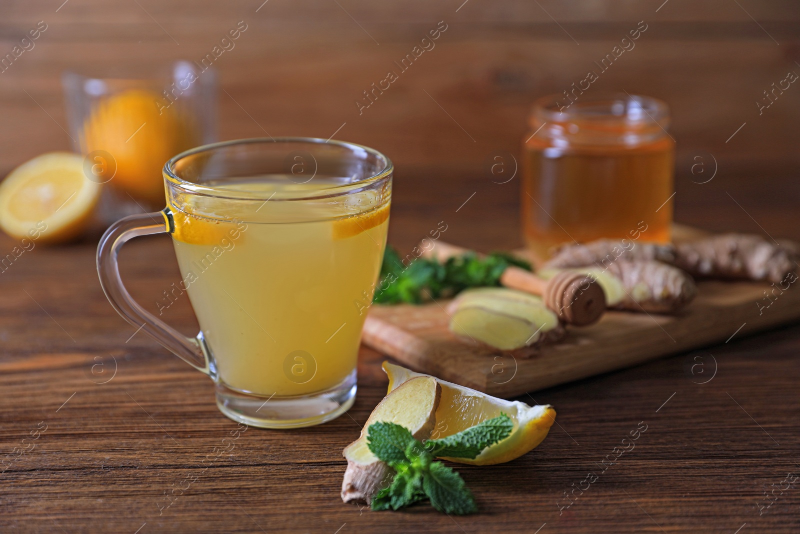 Photo of Glass of aromatic ginger tea and ingredients on wooden table, closeup