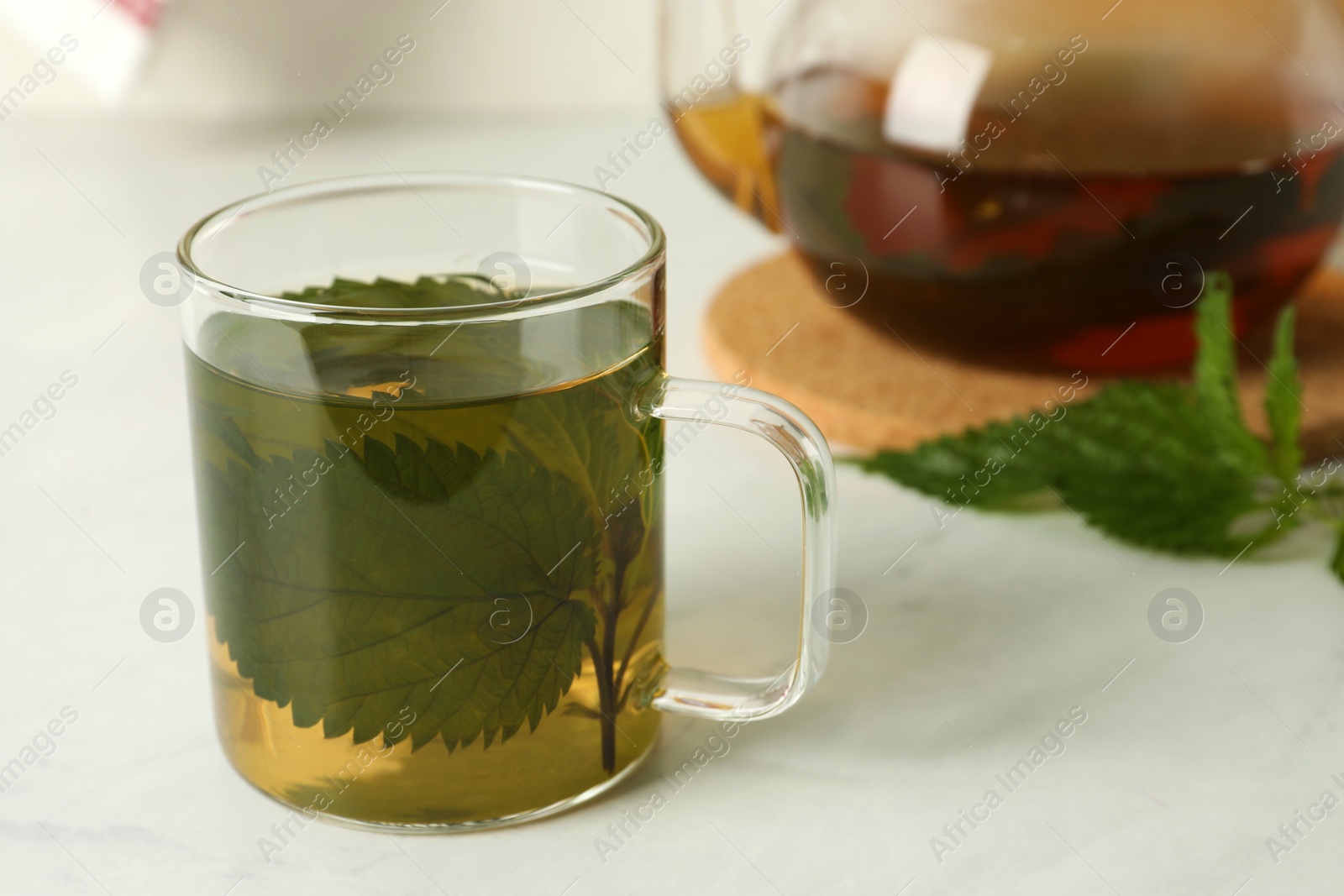 Photo of Glass cup of aromatic nettle tea on white table, space for text